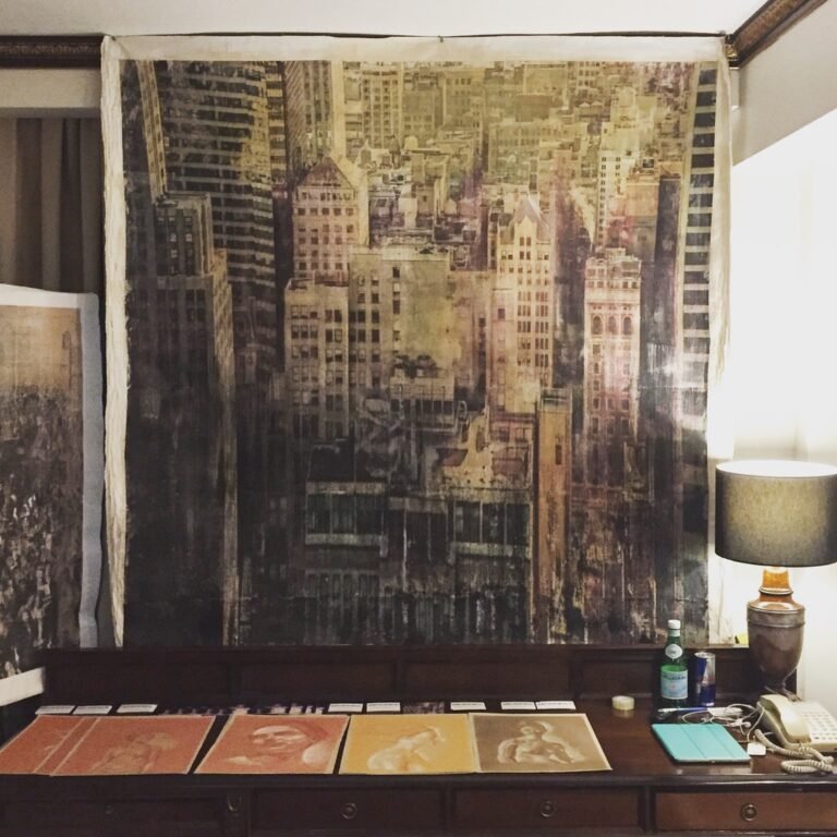 Large cityscape by Dario Moschetta hung above a desk with drawings, Artrooms London 2018