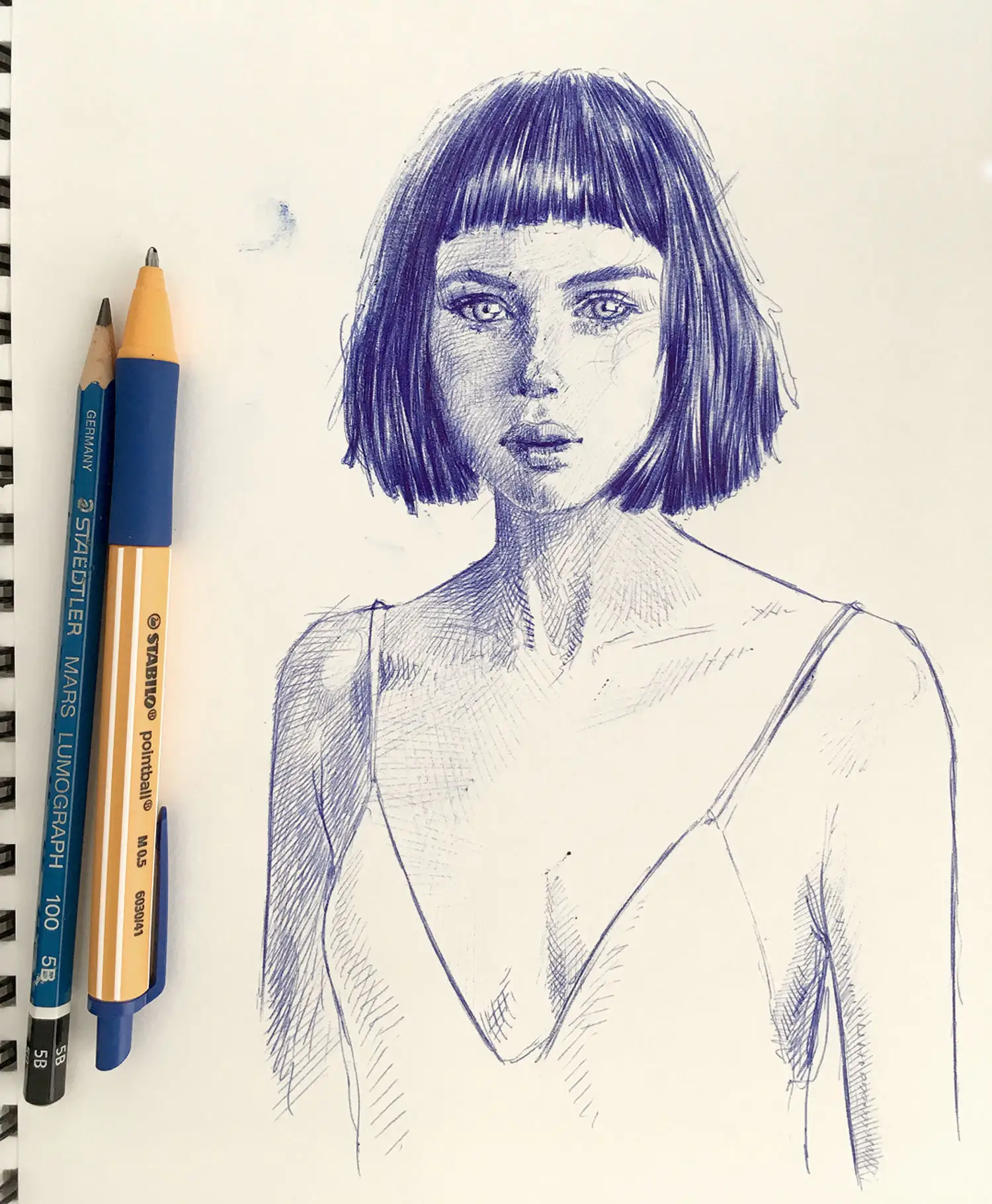 Blue ballpoint portrait drawing with pencils beside the artwork – original female portrait on paper