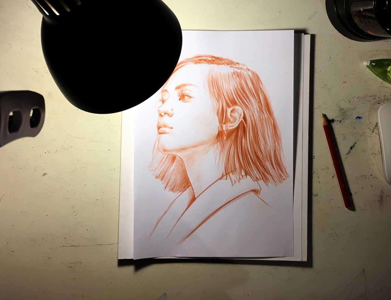 Work in progress view of “Terracotta Light” – red pastel female portrait drawing under studio light
