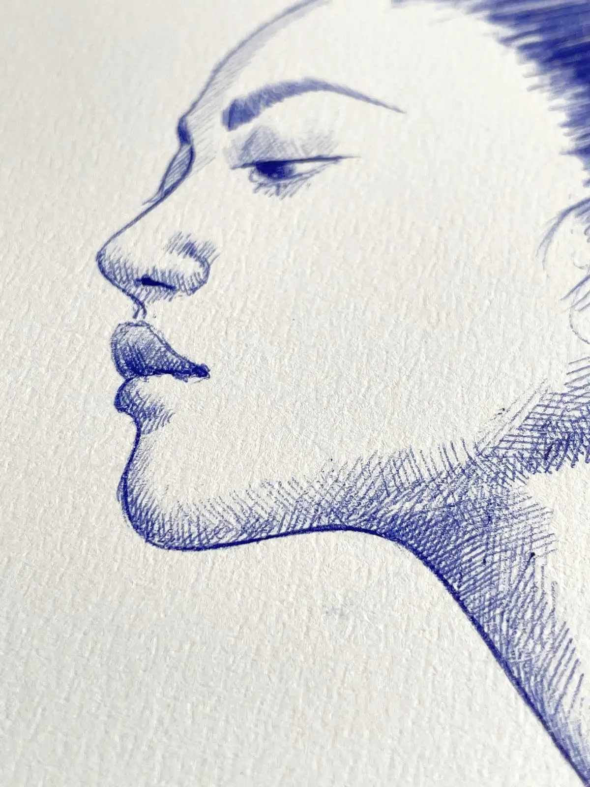 Close-up of a female portrait in blue ballpoint ink on A4 paper, focusing on the side profile with detailed facial features