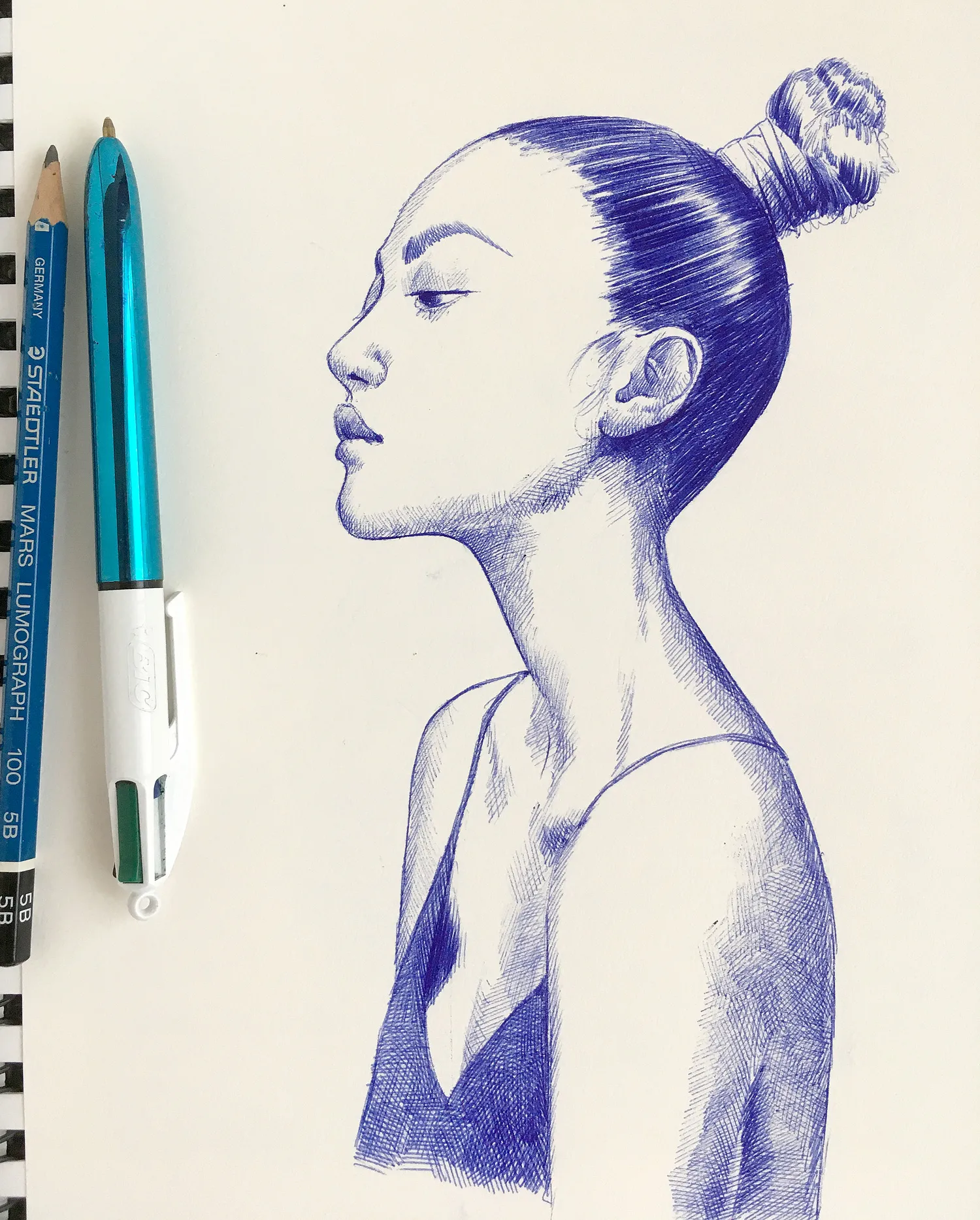 Female portrait in blue ballpoint ink on A4 paper, displayed on a table with natural light accentuating the details